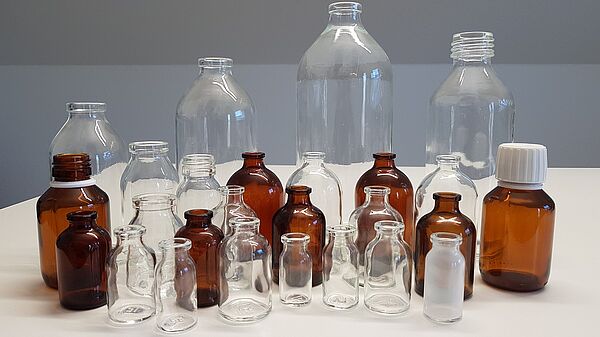 Viele Hüttenglas Flaschen von SGD nebeneinander in klar und braun auf einem Tisch